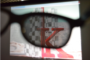 【2x3Dによる視聴の様子：裸眼では左目用2D映像，眼鏡越しには右目用映像が見えており，二重像は見えない】